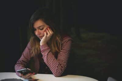 woman leaning on white wooden table while holding black Android smartphone